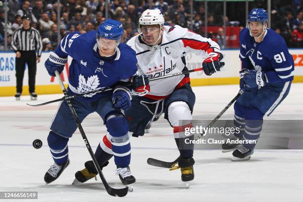 Alex Ovechkin of the Washington Capitals holds up Rasmus Sandin of the Toronto Maple Leafs from getting the puck during an NHL game at Scotiabank...