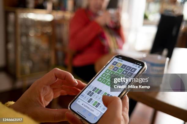 Woman plays Wordle alongside her mother on her smartphone at the kitchen table of her home and struggles to find the correct final word on 21st...