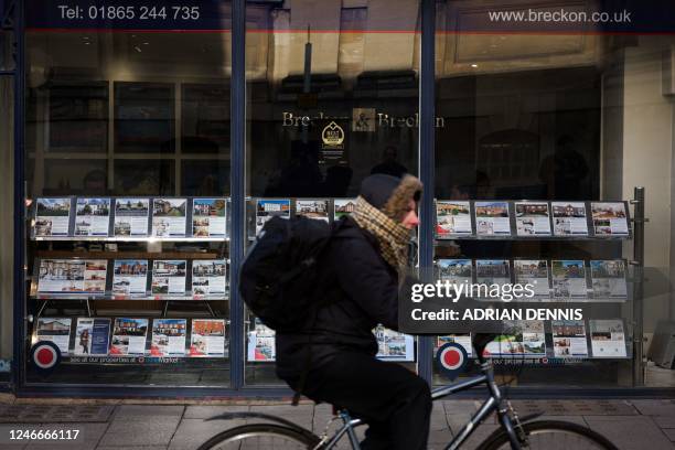 Cyclist passes in front of the front window of a real estate agency displaying a selection of properties to buy or rent, in Oxford, on January 30,...