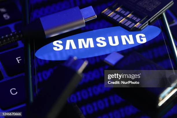 Samsung logo displayed on a phone screen with a binary code reflected on it, a laptop keyboard, a memory card, an adaper and cables are seen in this...