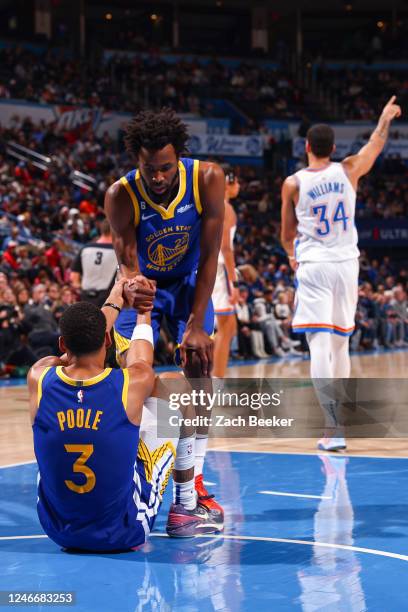 Andrew Wiggins helps Jordan Poole of the Golden State Warriors up during the game on January 30, 2023 at Paycom Arena in Oklahoma City, Oklahoma....