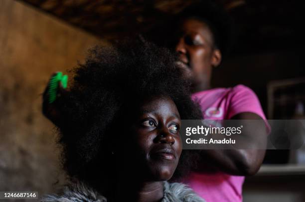 An African woman gets her hair braided at a tin hair salon in Kibera, the second largest slum of Africa in Nairobi, Kenya on January 19, 2023. Hair...