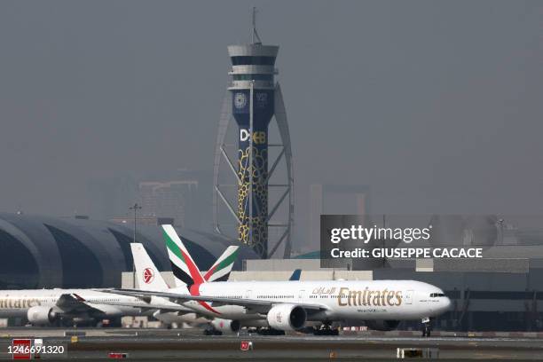 An Emirates Boing 777-300ER is pictured in front an air traffic control tower at Dubai International Airport in Dubai , on January 30, 2023.