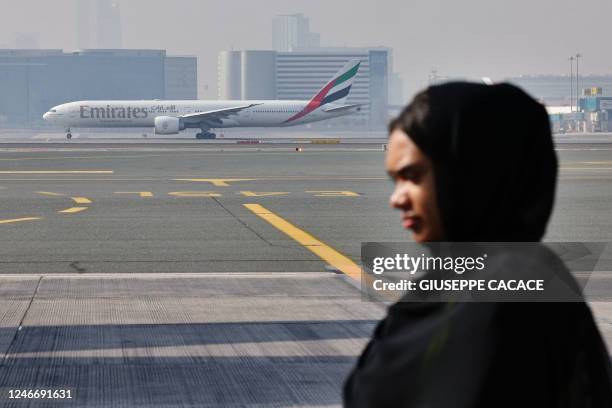 An Emirati woman stands in front of an Emirates Boing 777-300ER taxing at the tarmac of Dubai International Airport in Dubai, on January 30, 2023.