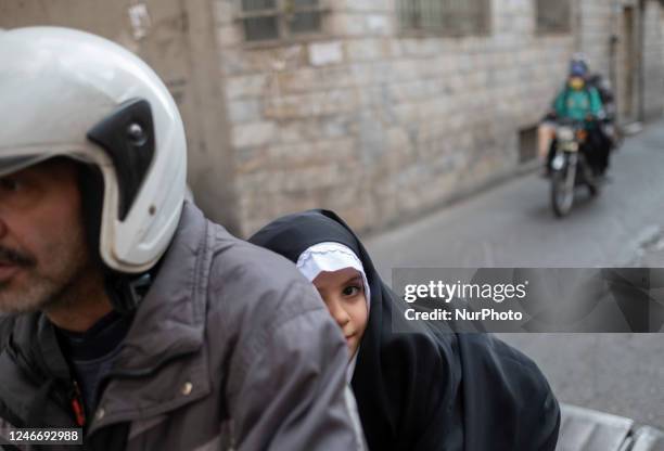 Veiled schoolgirl sits on her father's motorcycle as she rides out of a school in southern Tehran, January 29, 2023. Since the Iranian Islamic...