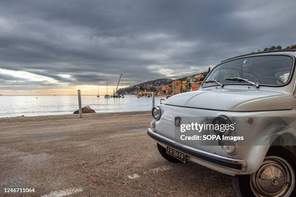 An old white Fiat 500 is parked along the promenade of Villefranche-sur-Mer during off-season.