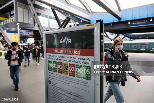 Commuters walk behind a board warning about an industrial action as part of a national strike, at the Reading train station, on February 1, 2023. -...