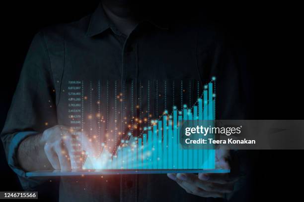 a male businessman is standing by a tablet analyzing the ongoing upwards of the graph. a rapidly changing business concept on a black background. - overdracht business mensen stockfoto's en -beelden