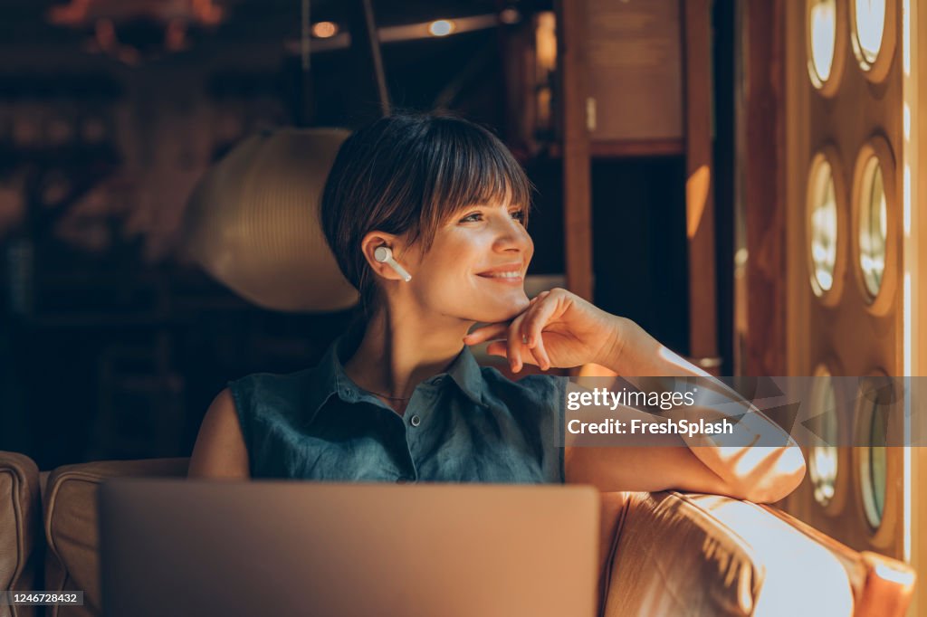 Mujer feliz usando un ordenador portátil y auriculares inalámbricos mientras trabajaba en un café