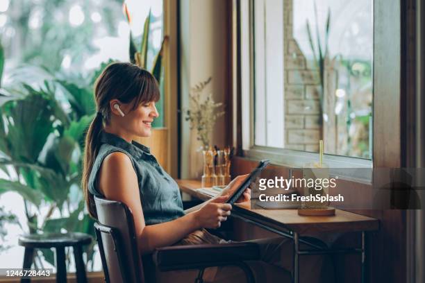lächelnde geschäftsfrau mit drahtlosen kopfhörern beobachten etwas auf einem digitalen tablet - ipad kopfhörer stock-fotos und bilder