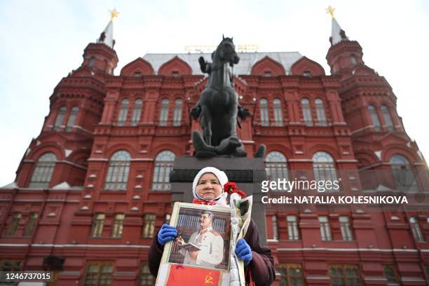 An elderly woman holding a portrait of Soviet leader Joseph Stalin and red carnations stands in front of the monument to Marshal Georgy Zhukov as...