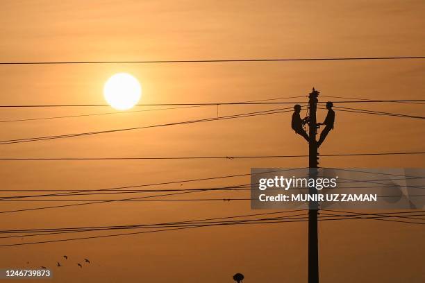 Electricians carry out maintenance work on transmission lines on an electric pole in the backdrop of the setting sun in Dhaka on February 2, 2023.