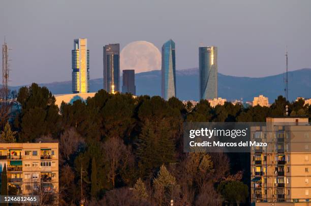 The full moon of February known as Snow moon sets over the skyline with the skyscrapers of the Four Towers Business Area of Madrid.