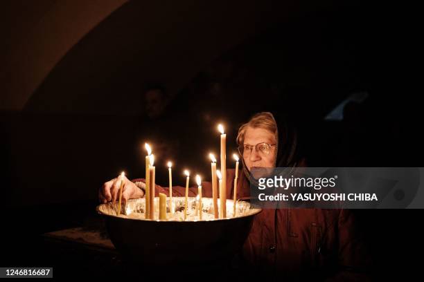 An Orthodox Christian lights a candle during the Sunday prayer at the basement of the Church of All Saints as sounds and vibrations of shelling...