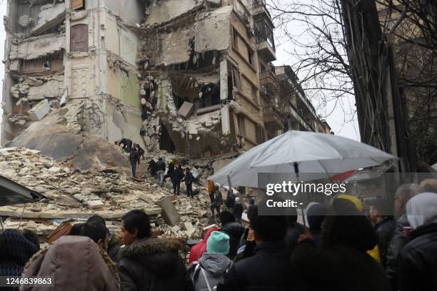 Onlookers watch as rescue teams look for survivors under the rubble of a collapsed building after an earthquake in the regime-controlled northern...