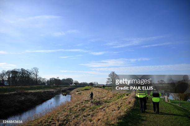 Lancashire police officers walk along the riverbank as a team from Specialist Group International travel aboard a RIB using sonar to scan the bed of...