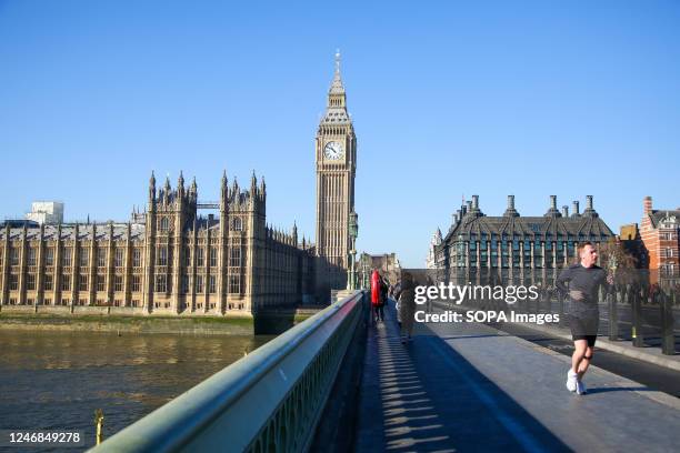 Man seen running on Westminster Bridge with a view of Big Ben and the Houses of Parliament on a sunny day in London.