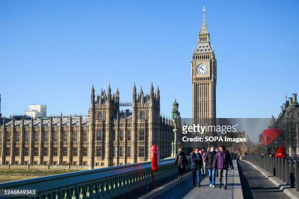 People on Westminster Bridge with a view of Big Ben and the Houses of Parliament on a sunny day in London.
