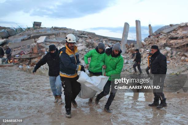 Graphic content / TOPSHOT - Syrian rescuers carry a body past the collapsed buildings on February 6, 2023 in the town of Sarmada, in Syria's...