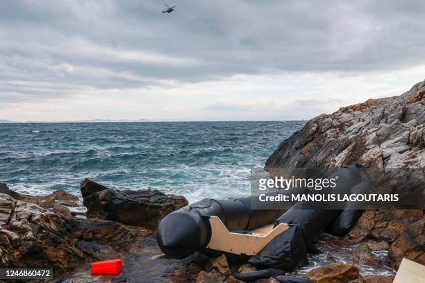 Rescue helicopter flies over the sea close to where a rubber boat, believed to be used by migrants, lies destroyed on the rocky shoreline, in Thermi...