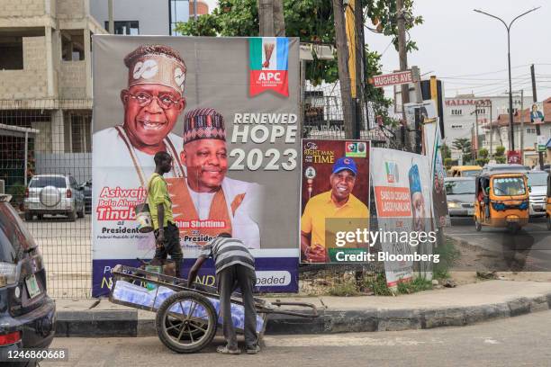 Worker arranges bags of water onto a cart in front of election posters for the All Progressive Congress presidential candidate Bola Tinubu and his...