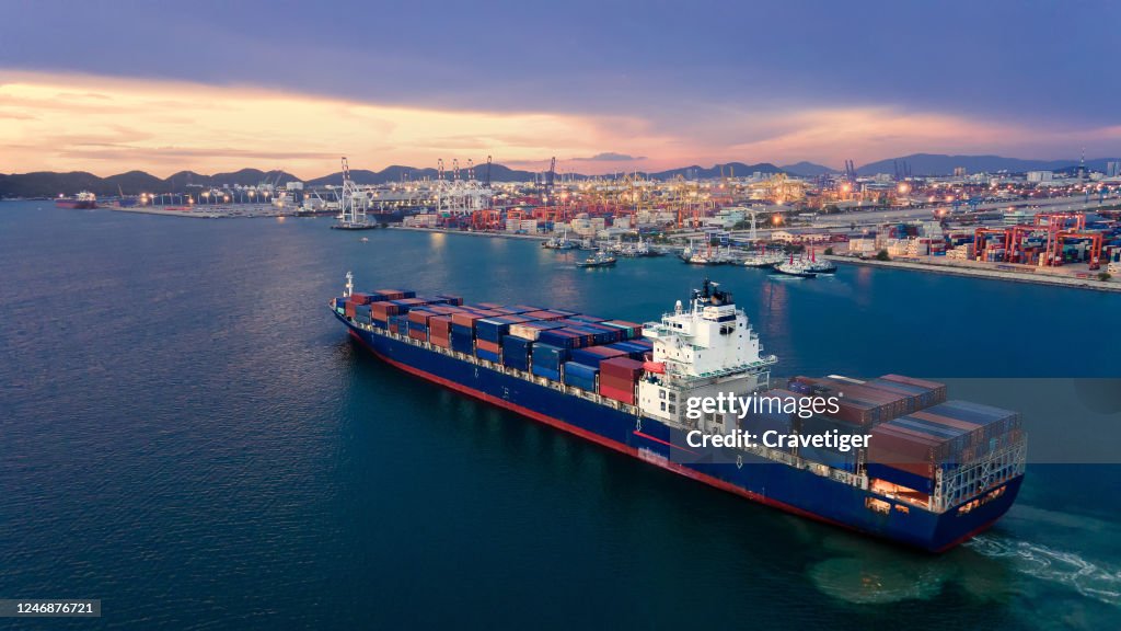 Aerial view drone shot of a massive vessel in dock at the Port of Thailand, full of multicoloured shipping containers. Boat 're going to push and pull Ship with container to deep sea.