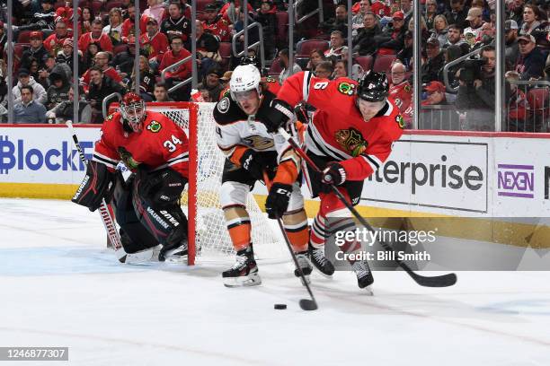 Max Comtois of the Anaheim Ducks and Jake McCabe of the Chicago Blackhawks battle for the puck next to goalie Petr Mrazek of the Chicago Blackhawks...