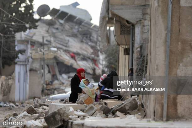 Syrian women and children sit wrapped in blankets outside collapsed buildings on February 7 in the town of Jindayris, in the rebel-held part of...