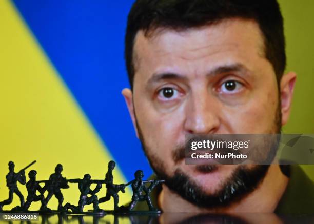 Illustration with figures of soldiers, seen in front of a photo of Volodymyr Zelenskiy, President of Ukraine, displayed on a computer screen. On...