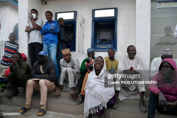 People sit to queue early in the day to withdraw money from cash dispensers that is crippled by cash shortages at a bank in Kano, northwest Nigeria,...