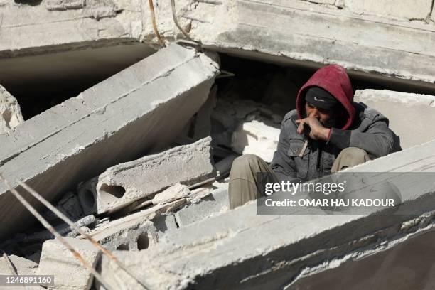 Syrian man sits amidst the rubble as he waits for new about family members stuck under the wreckage in the town of Harim in Syria's rebel-held...