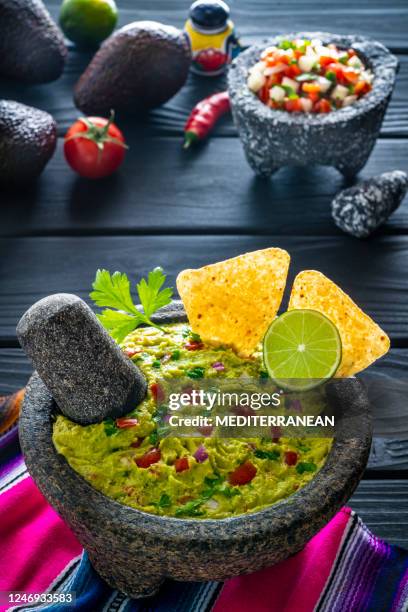 guacamole avocado mexican recipe in stone molcajete with ingredients on black wood - mexican food on table stock pictures, royalty-free photos & images
