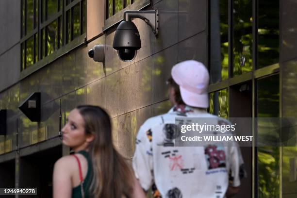 People walk past a security camera in Melbourne on February 9, 2023. - Australia's defence department will strip its buildings of Chinese-made...