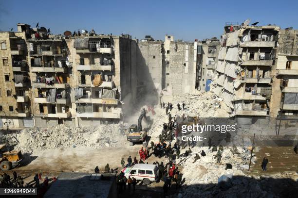 Syrian soldiers look on as rescuers use heavy machinery sift through the rubble of a collapsed building in the northern city of Aleppo, searching for...