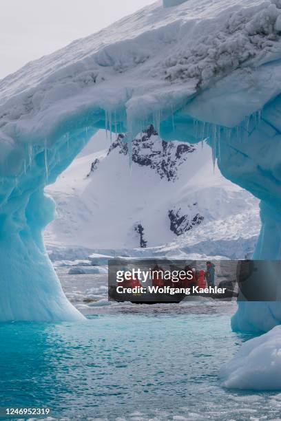 Tourists in a zodiac exploring an iceberg arch in Cierva Cove, a cove along the west coast of Graham Land, Antarctic Peninsula, Antarctica.