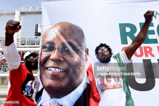 Supporters gesture next to the banner of the candidate of the opposition Peoples Democratic Party Atiku Abubakar during a campaign rally in Kano,...