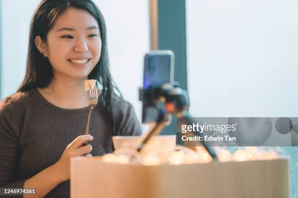 una adolescente china asiática vlogging en su habitación comiendo manzana usando su teléfono inteligente durante el día de lluvia sonriendo - sólo chicas adolescentes fotografías e imágenes de stock