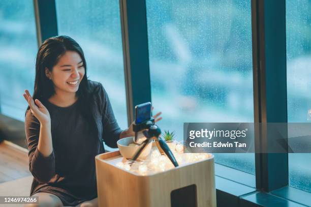 eine asiatische chinesische teenager-mädchen vlogging in ihrem zimmer essen apfel mit ihrem smartphone während regen tag lächelnd - girl smiling on rain stock-fotos und bilder