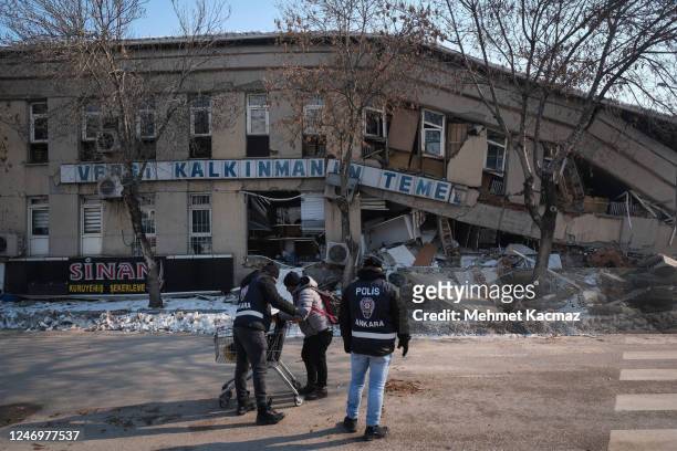 Policemen check a local man to prevent potential looting in front of ruined Elbistan Tax Office building on February 10, 2023 in Elbistan Turkey. A...