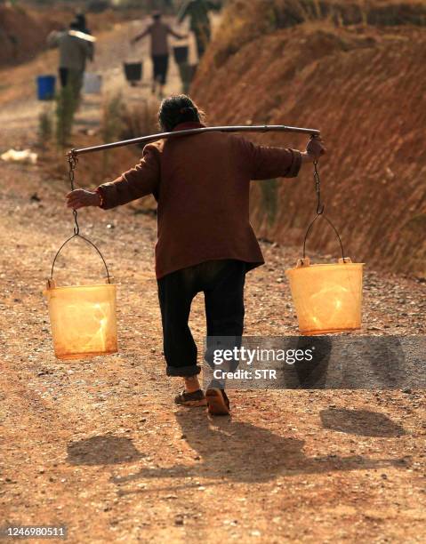 Chinese villagers carry pails of water they collected from a well, back to their homes in Yiliang, southwest China's Yunnan province on February 27,...