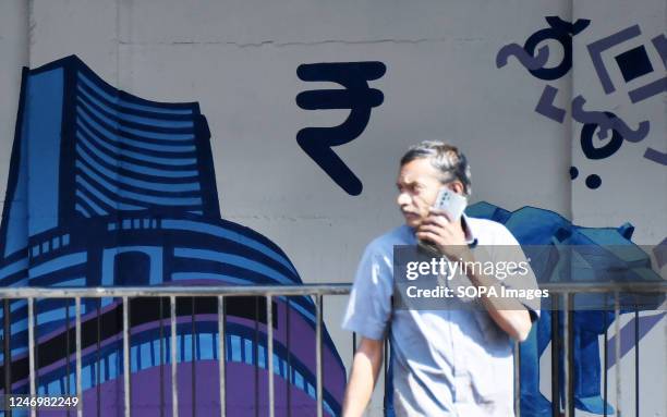Man is seen communicating on a mobile phone next to the mural about the Bombay Stock Exchange with an Indian Rupee symbol in Mumbai.