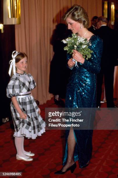 Princess Diana wearing a blue sequin gown by Catherine Walker with a young girl and a bouquet of flowers at the film premiere of "Biggles" at the...