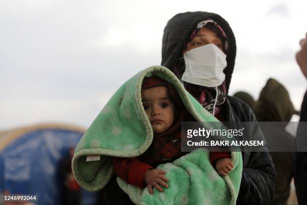 Woman carrying a baby watches as search and rescue operations continue days after a deadly earthquake hit Turkey and Syria, in the town of Jindayris,...