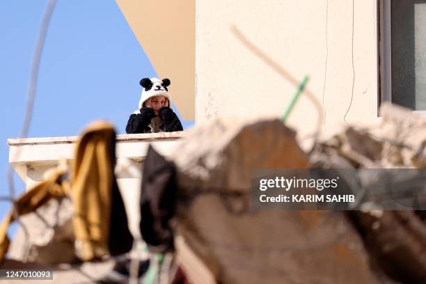 Young resident of a still standing building watches continuing search operations amidst the rubble of a collapsed building in the regime-controlled...