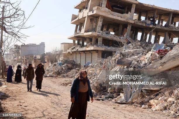 Residents walk along destroyed buildings, as search and rescue operations continue days after a deadly earthquake hit Turkey and Syria, in the town...