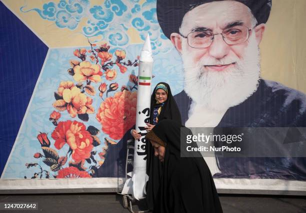 An Iranian schoolgirl is holding a model of the Iranian-made Zolfaghar missile while standing in front of a giant portrait of Iran's Supreme Leader,...