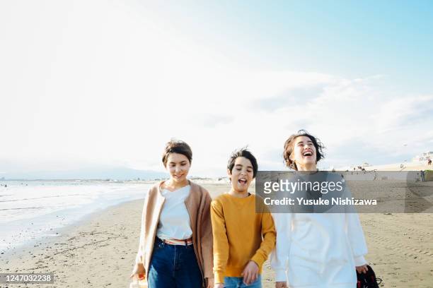 three teenagers walking together on sandy beach - three girls at beach stock pictures, royalty-free photos & images