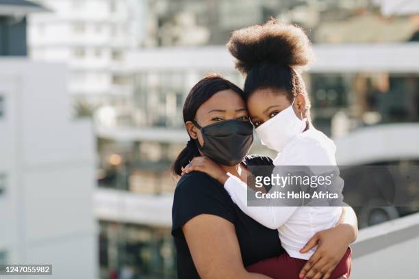 Beautiful & delighted daughter and mother wearing black and white face masks on a rooftop