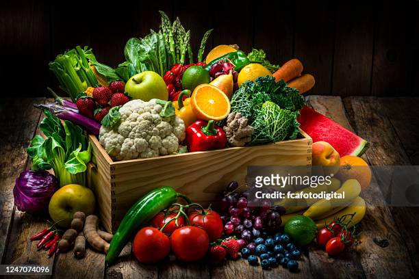 crate filled with a large selection of healthy fresh organic fruits and vegetables shot on dark wooden table - vegetable stock pictures, royalty-free photos & images