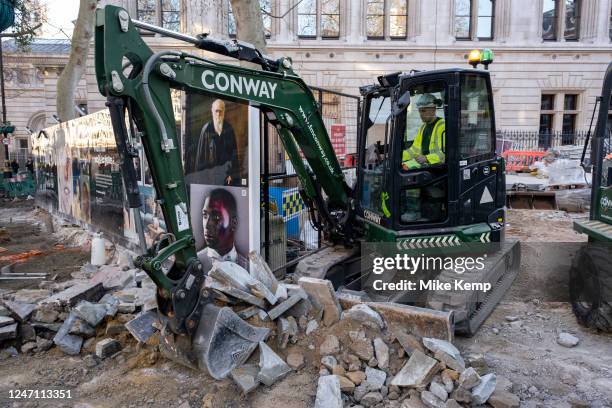 Worker operating a small digger interacts with classic portraits of well known or famous people from contemporary culture including Charles Darwin...